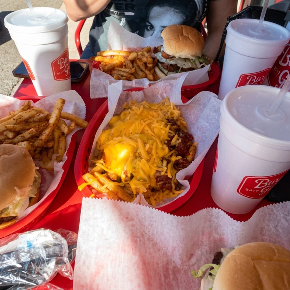 Burger Girl burgers, seasoned fries, cheese-topped chili fries, and fountain drinks served on red trays at an outdoor table.